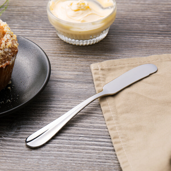 A plate with a Walco stainless steel butter spreader and a muffin on a napkin.