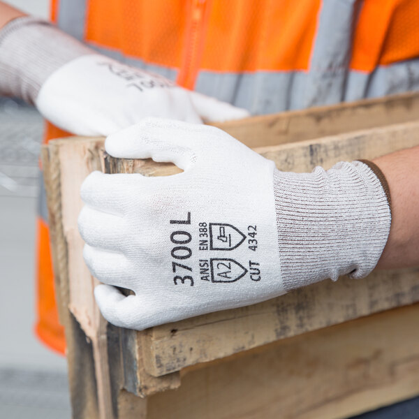 A person wearing Cordova white HPPE gloves with white polyurethane palm coating holding a wooden box.