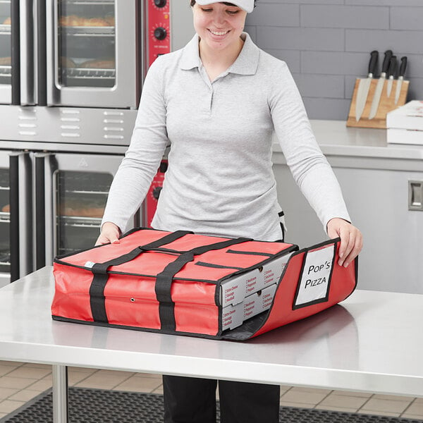 A woman in a chef hat holding a red Choice insulated pizza delivery bag.