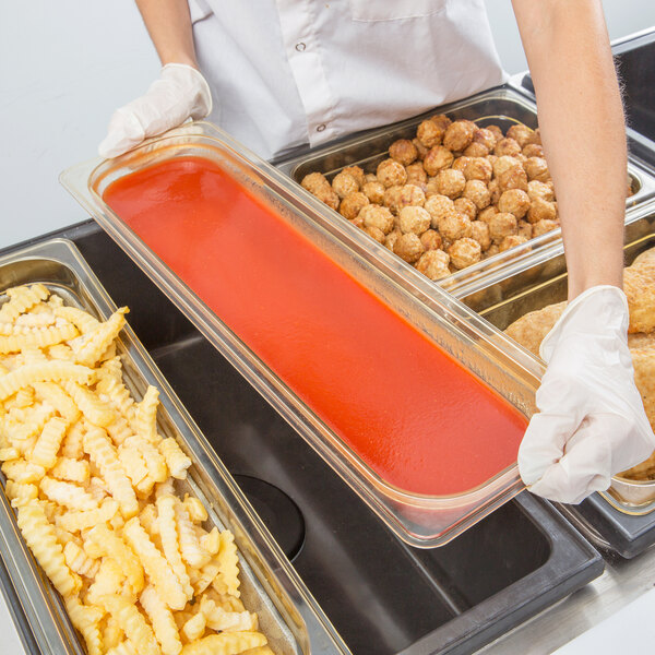 A person in white gloves holding a Cambro amber high heat plastic food pan full of food.
