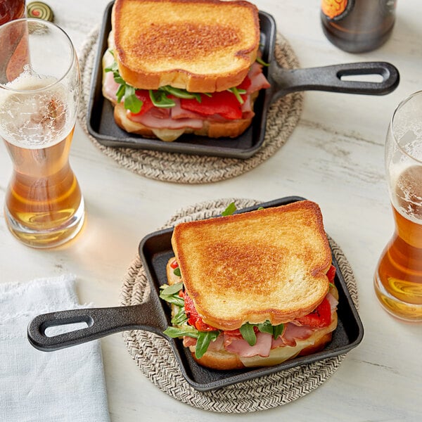 Two Valor mini cast iron pans with toasted sandwiches and two glasses of beer.