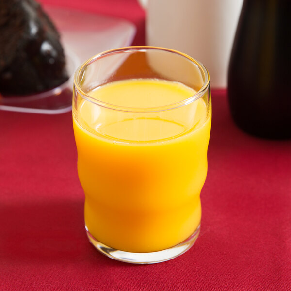 A Libbey beverage glass filled with orange juice on a red table.