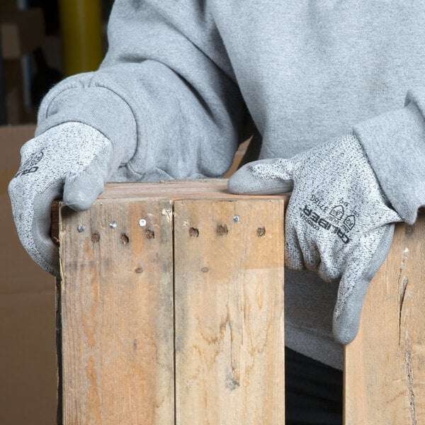 A person wearing Cordova Caliber gray warehouse gloves holding a piece of wood.
