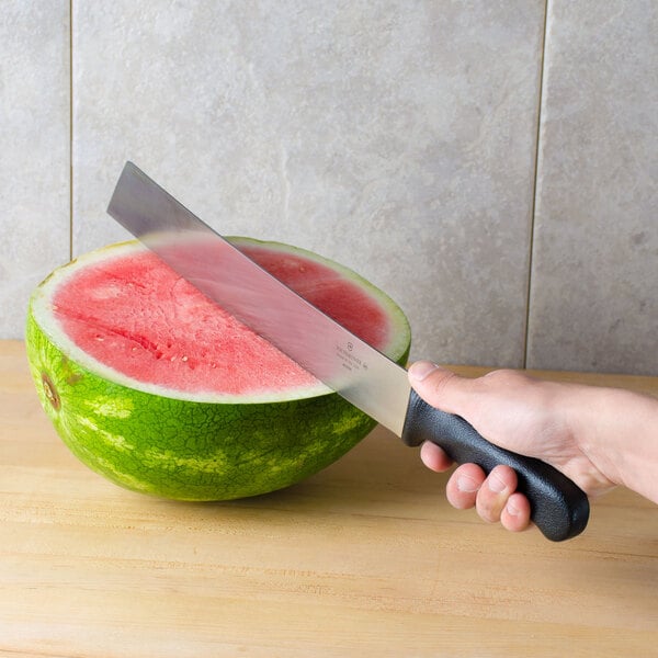 A hand using a Victorinox Watermelon Knife to cut a watermelon on a kitchen counter.
