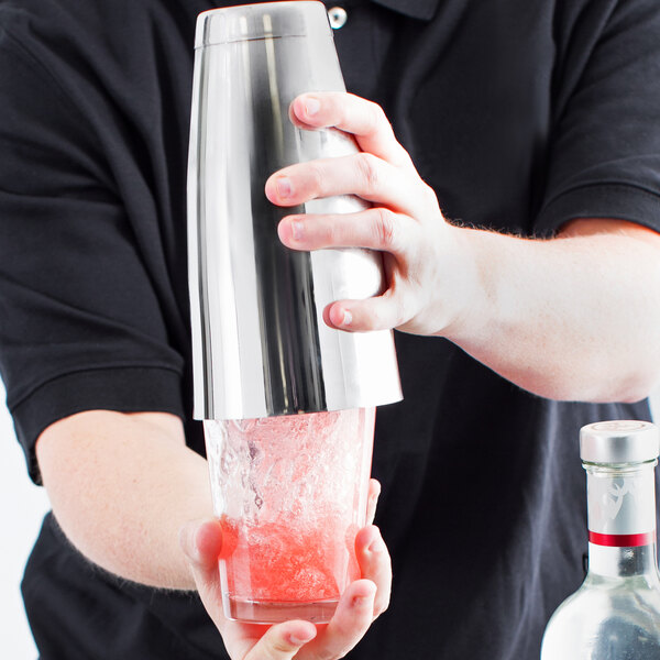 A person using a Vollrath stainless steel cocktail shaker to make a drink.