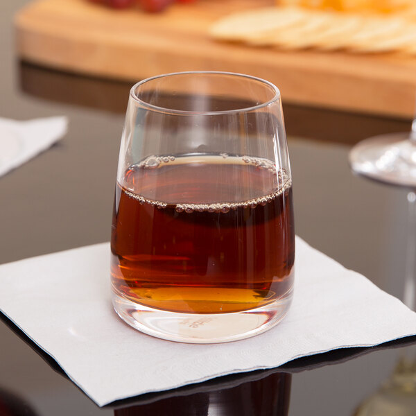 A Stolzle Experience juice glass of brown liquid on a white table with a black border