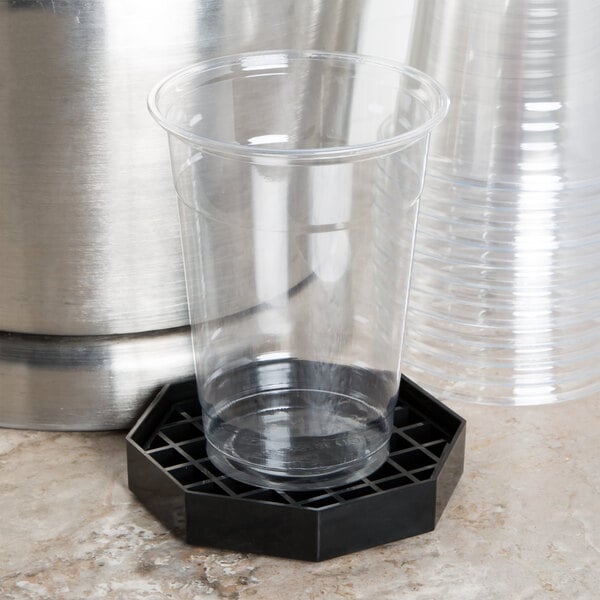 A clear plastic cup on a black Choice octagonal drip tray.