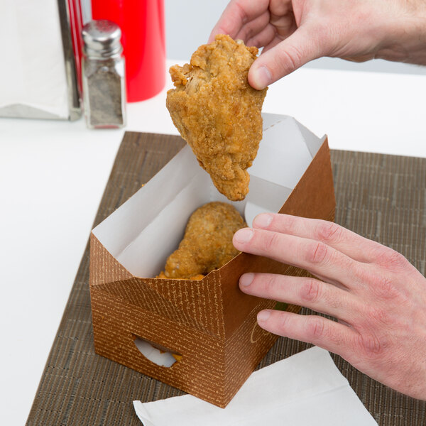 A hand holding a piece of fried chicken in a Hearthstone take-out box.
