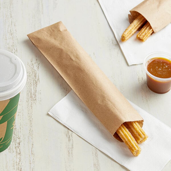 A Kraft paper bag with a container of liquid and churros inside.
