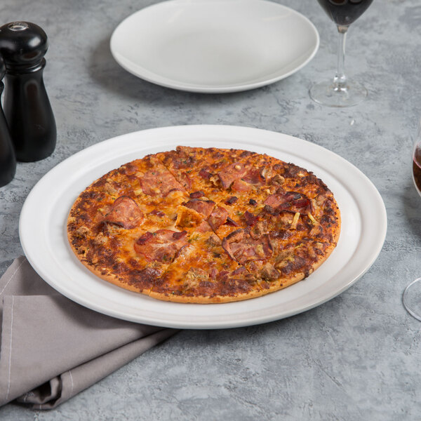 A pizza on an American Metalcraft white ceramic pizza serving tray with a glass of wine on a table.