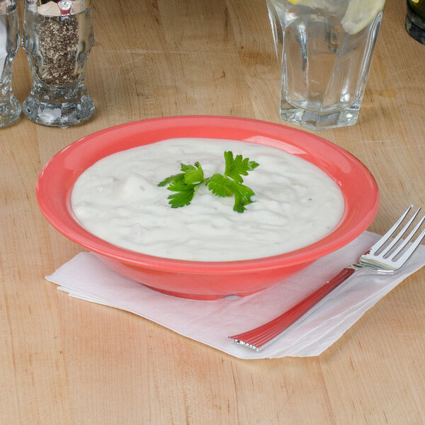 An orange Thunder Group melamine soup bowl filled with white soup and a green leafy garnish.