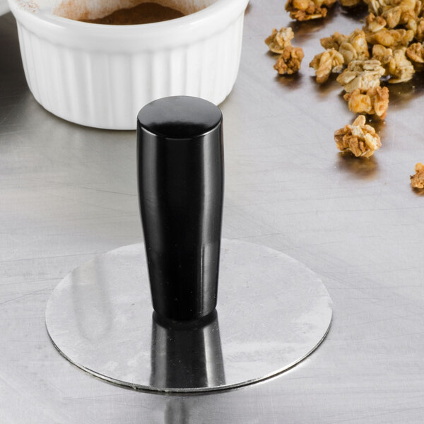 A Matfer Bourgeat stainless steel mold pack down tool with a black Bakelite handle in a metal stand next to a bowl of popcorn.