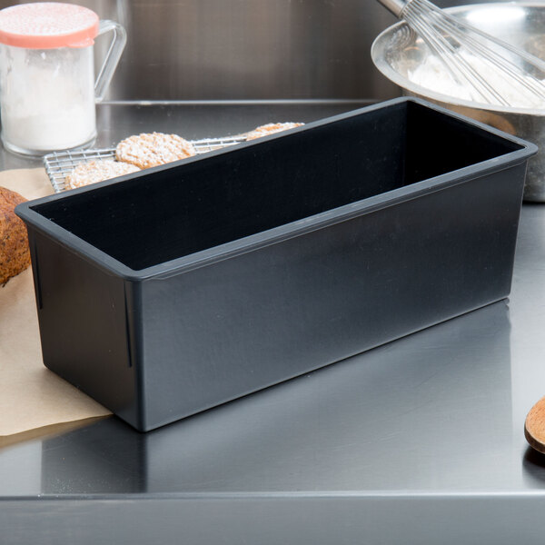 A black rectangular Matfer Bourgeat bread loaf pan on a counter with bread and other items.