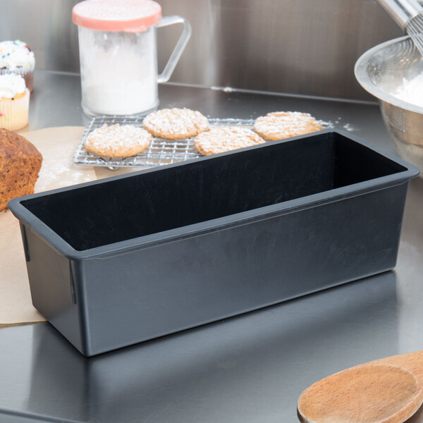 A black Matfer Bourgeat non-stick bread loaf pan on a counter with cookies and other items.