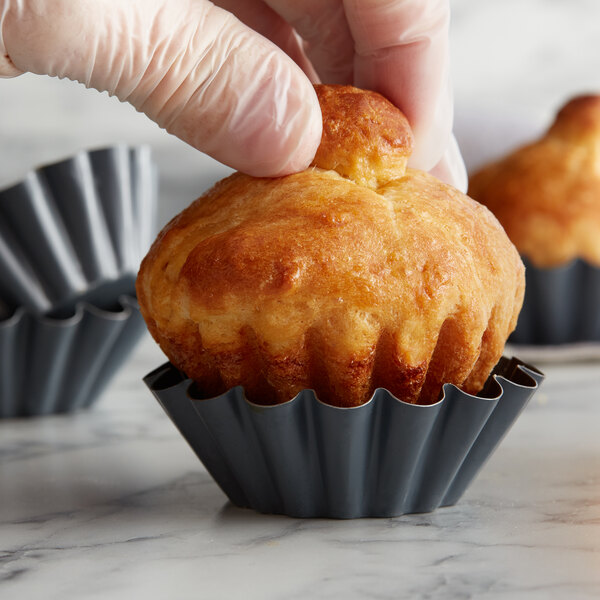 A hand placing a mini brioche in a grey fluted pan.