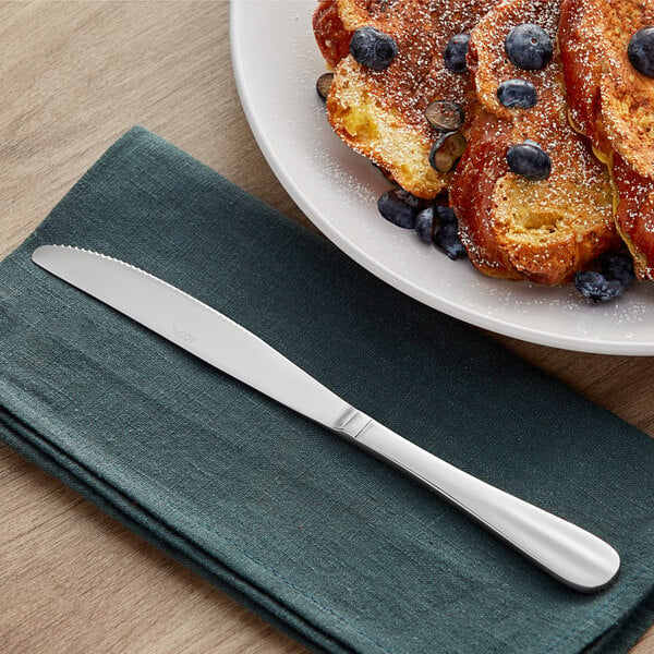 A table knife on a napkin next to a plate of French toast with blueberries and powdered sugar.