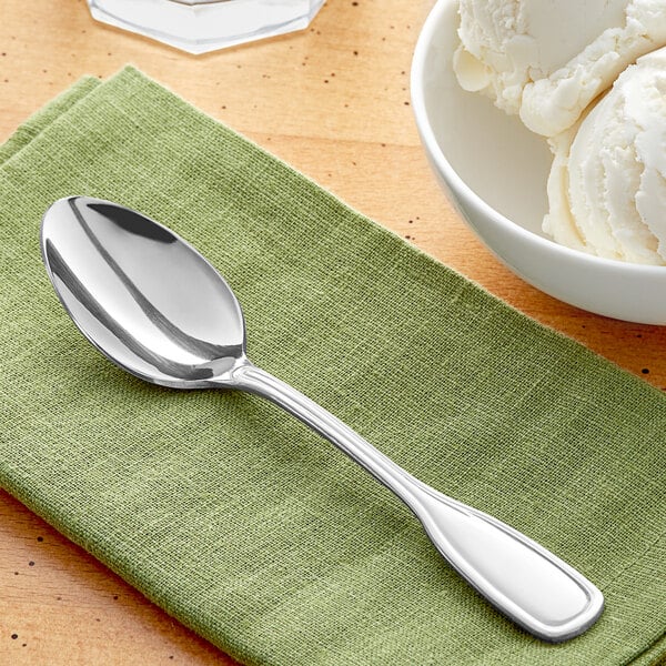 An Acopa Saxton stainless steel teaspoon on a green napkin next to a bowl of ice cream.