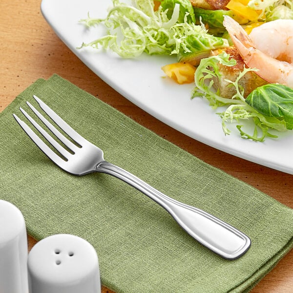 An Acopa Saxton stainless steel salad fork on a table with food.
