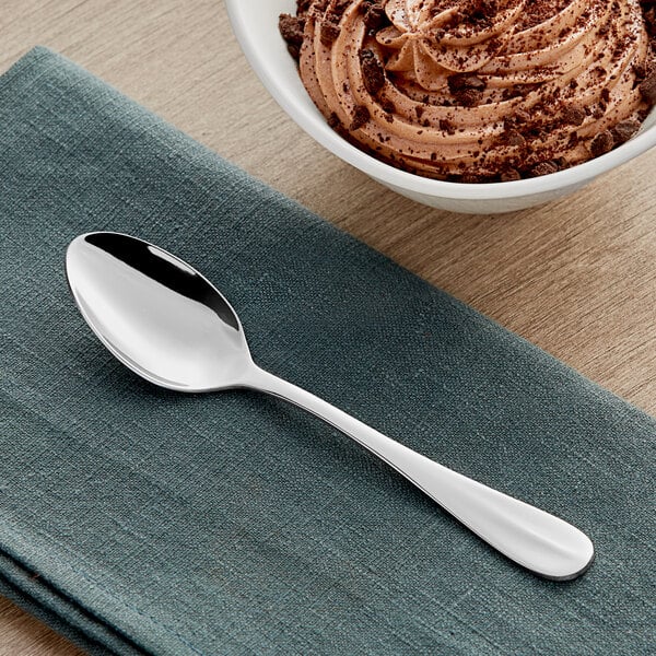 An Acopa Benson stainless steel teaspoon on a cloth next to a bowl of ice cream.