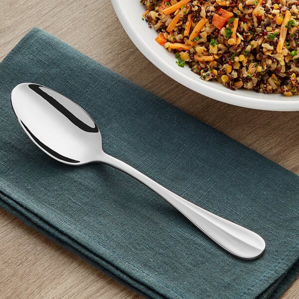 An Acopa Benson stainless steel serving spoon on a napkin next to a bowl of rice.