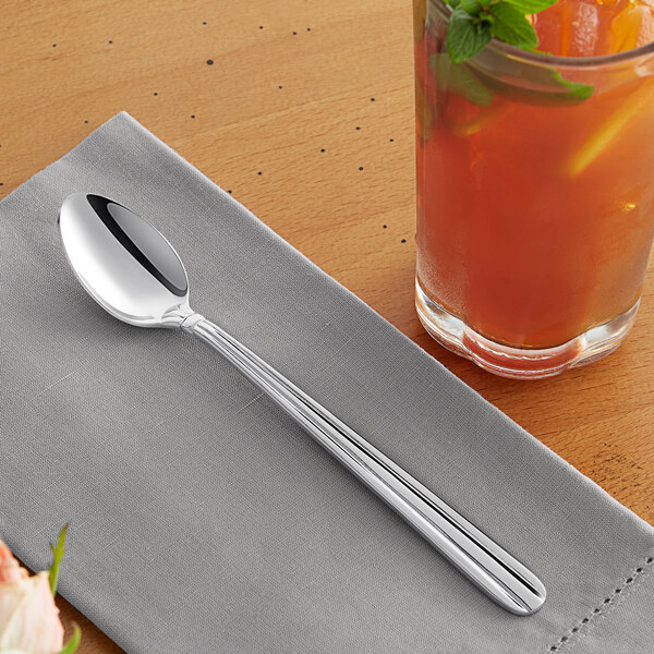 An Acopa stainless steel iced tea spoon on a napkin next to a glass of iced tea.