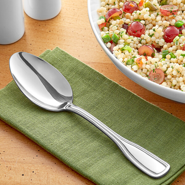 An Acopa Saxton stainless steel serving spoon on a table next to a bowl of food.