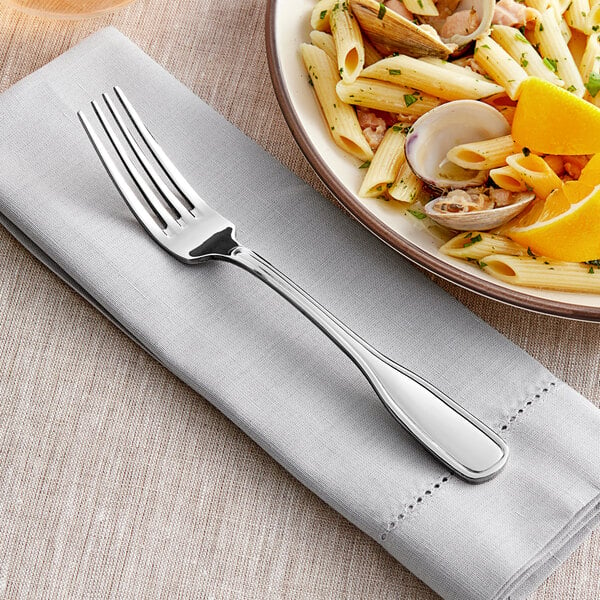 An Acopa stainless steel dinner fork next to a plate of pasta with clams and orange slices.