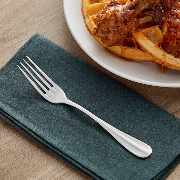 An Acopa Benson stainless steel table fork on a napkin next to a plate of food.