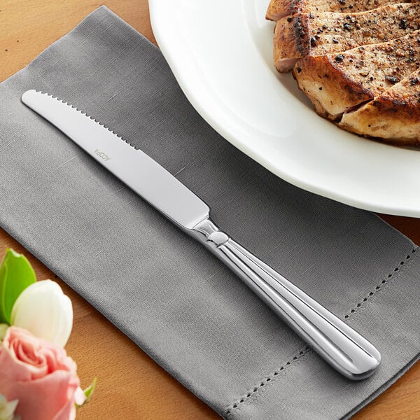 An Acopa Harmony stainless steel dinner knife on a napkin next to a plate of meat.