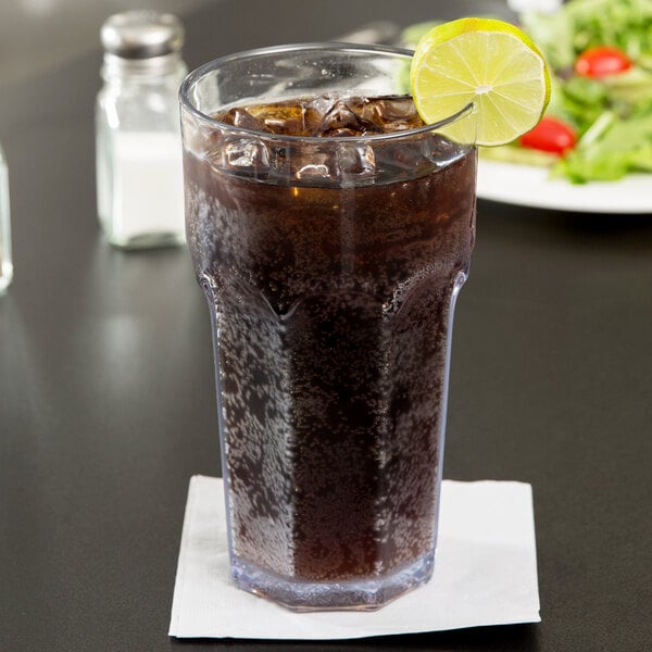 A Carlisle clear plastic tumbler of soda with ice and a lime wedge on the rim.
