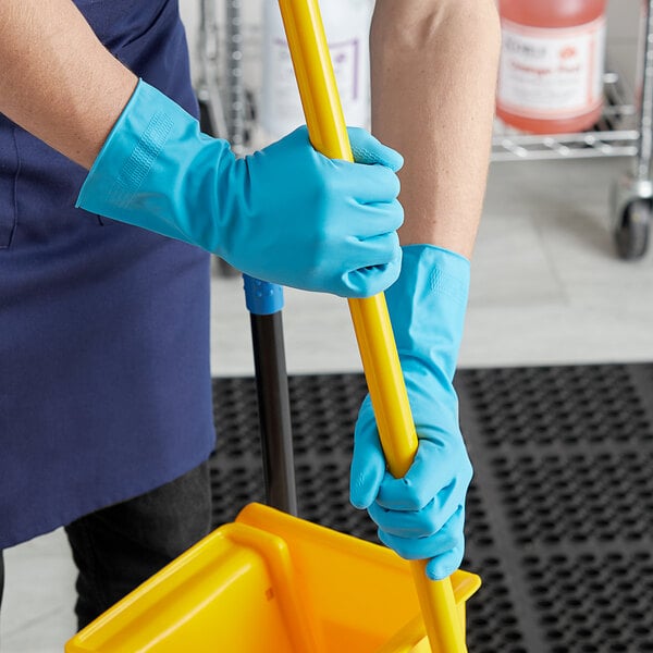 A person in blue Cordova Latex Rubber gloves with a yellow handle on a mop.