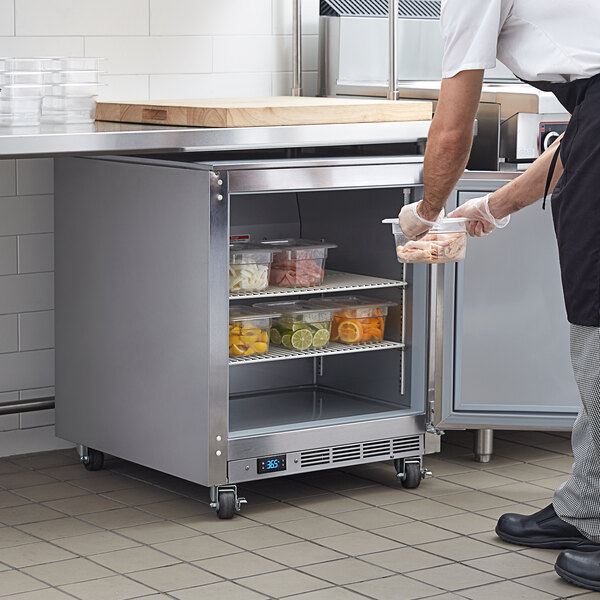 A man in a white shirt and black pants putting food into a Beverage-Air undercounter refrigerator in a school kitchen.