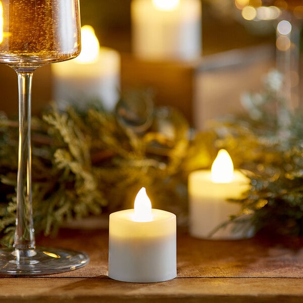 A wood table with a glass of wine and white Sterno flameless tea lights.
