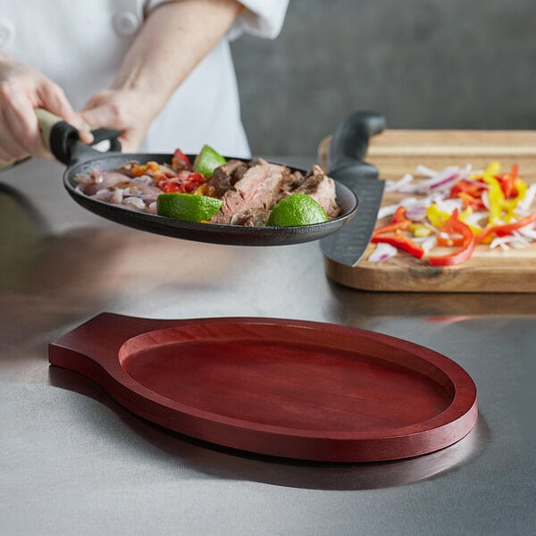 A chef using a mahogany Choice oval underliner to serve food from a skillet.