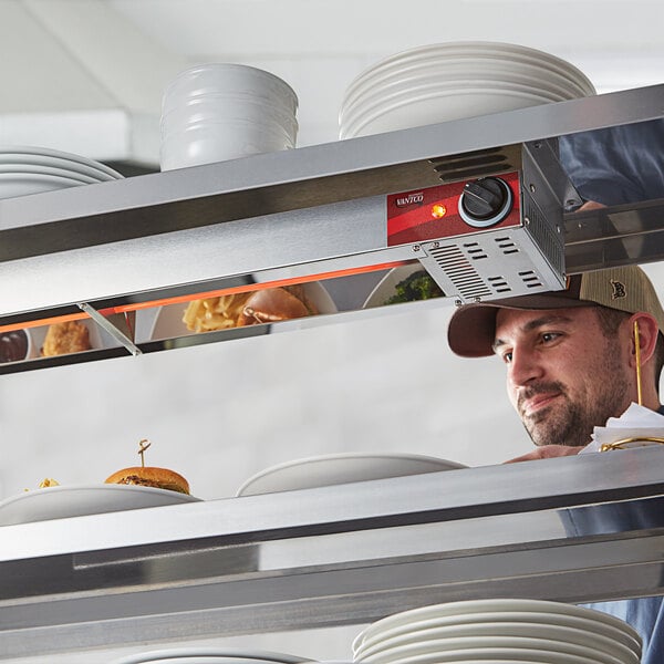 A man using an Avantco high wattage strip warmer on a counter in a professional kitchen.
