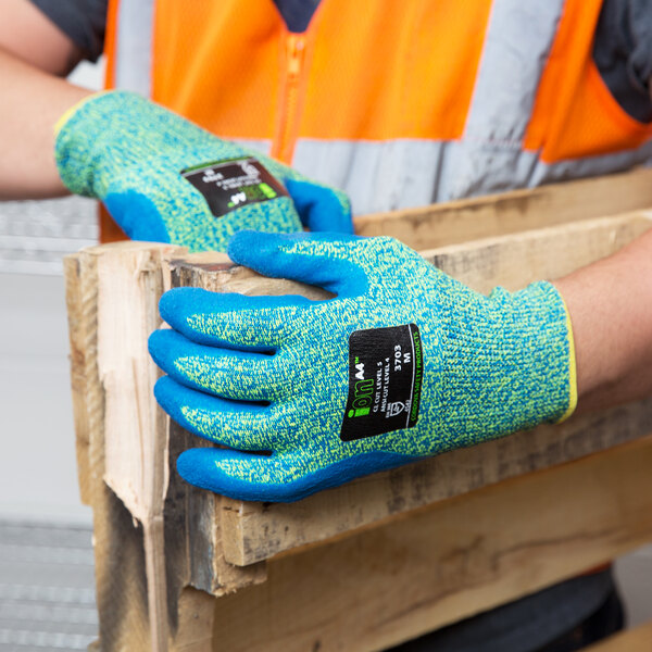 A person wearing blue Cordova iON cut resistant gloves with blue latex palms holding a piece of wood.