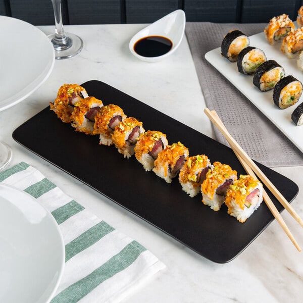 A rectangular matte black Acopa stoneware plate with sushi rolls and chopsticks.