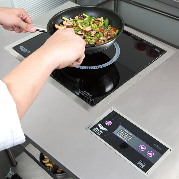 A hand cooking vegetables in a pan on a Vollrath Ultra Series drop in induction cooker.