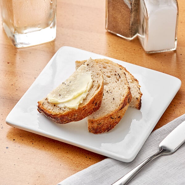 A piece of bread with butter on a white square plate.