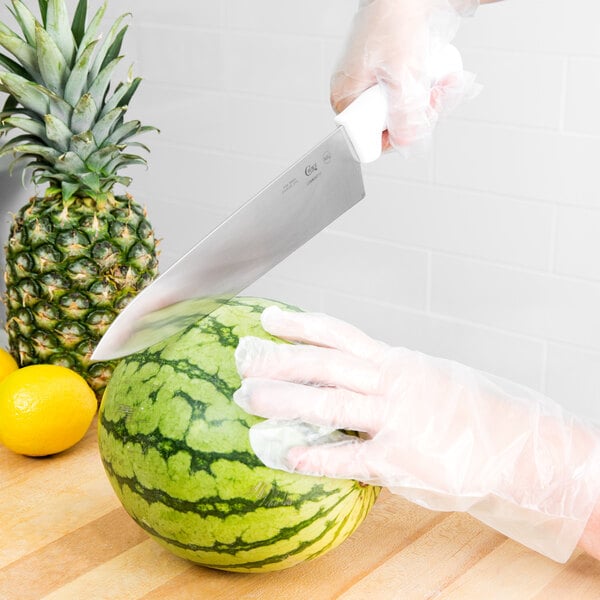 A person in gloves cutting a watermelon with a Choice chef knife.