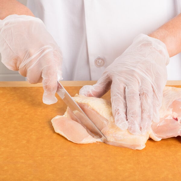 A person in white gloves using a Choice 6" Serrated Edge Utility Knife to cut raw chicken.