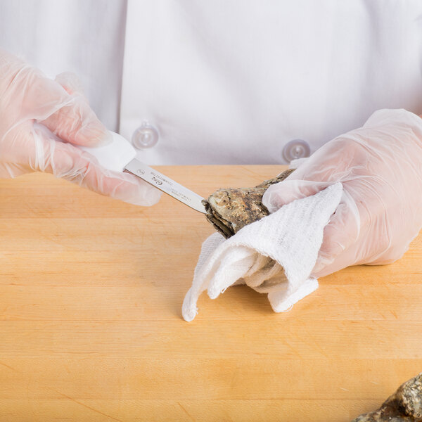 A person in white gloves using a Choice Providence Style Oyster Knife to cut an oyster.
