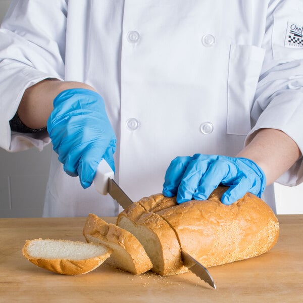 A person in blue gloves using a Choice curved serrated bread knife to cut a loaf of bread.