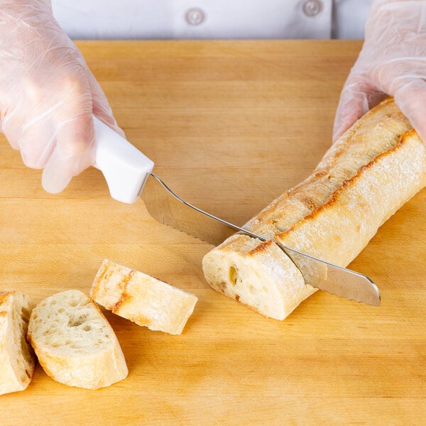 A gloved hand uses a Choice serrated bread knife with a white handle to cut bread.