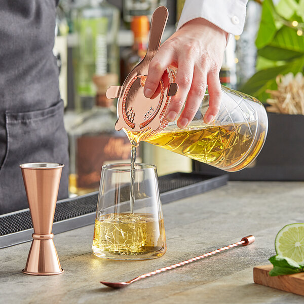 A bartender pouring liquid from a glass bottle into a cocktail stirring glass.