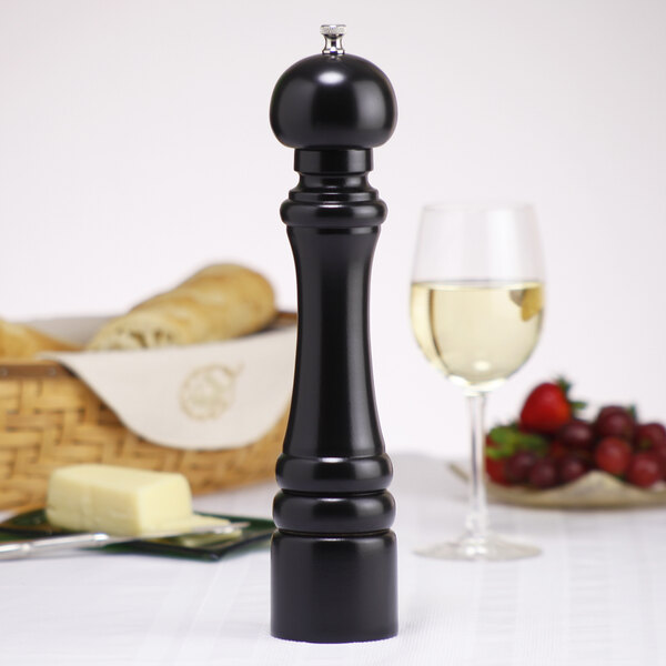 A black Chef Specialties President Ebony pepper mill next to a glass of white wine.