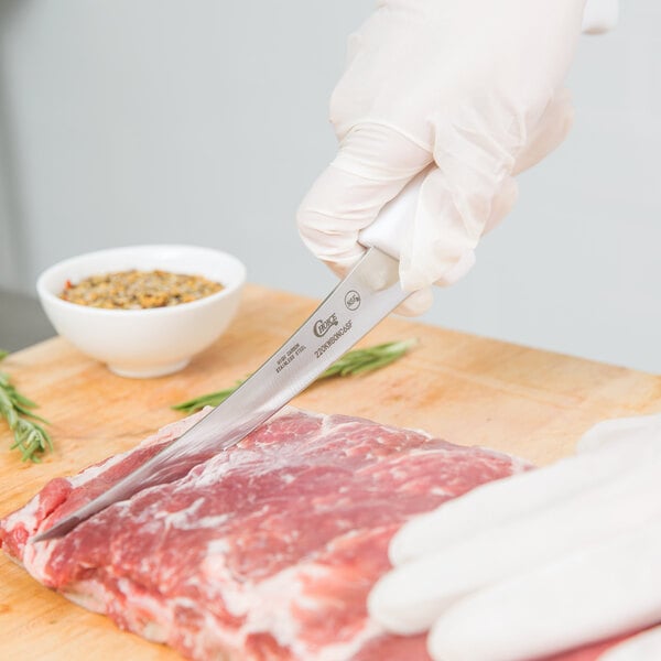 A person in white gloves using a Choice curved stiff boning knife to cut meat on a cutting board.