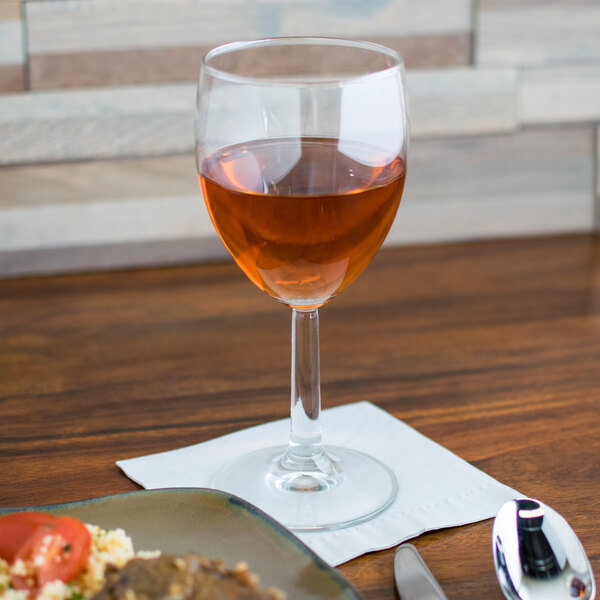 A Arcoroc wine glass of wine on a table next to a plate of food.