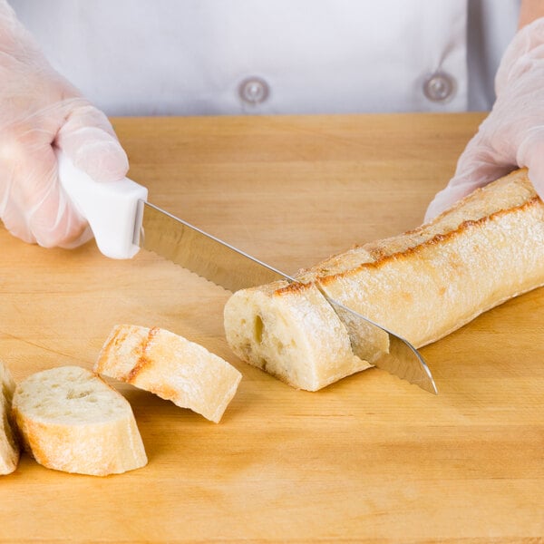 A person wearing gloves uses a Choice serrated bread knife to cut a piece of bread.