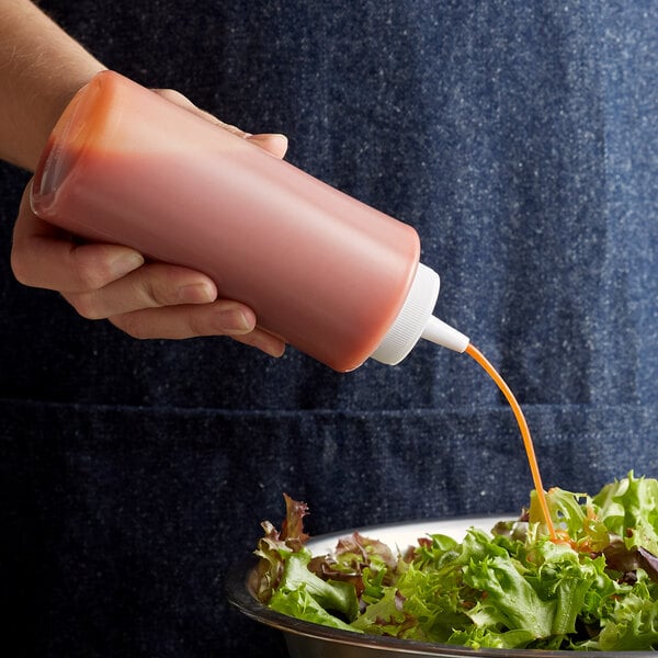 A person using a Choice clear squeeze bottle to pour sauce onto a salad.